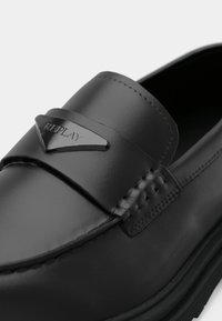 Sort læderloafer med en blank finish, der har et syet design, en central rem og en accent med sølvfarvet logo.
