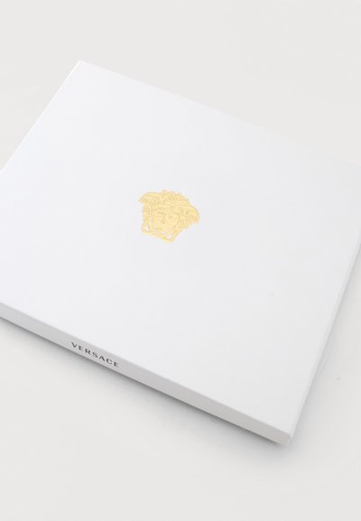 Boîte rectangulaire blanche Versace avec un logo tête de Méduse doré en relief au centre sur une surface claire.