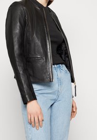 Svart läderjacka med rundad krage, framtill dragkedja och sidofickor; kombinerad med en svart topp och ljusblå högmidjade jeans.