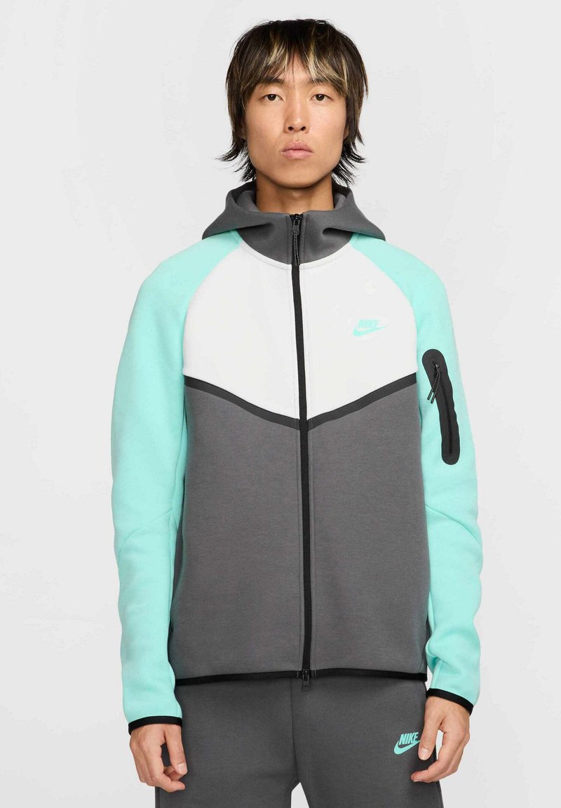 Sudadera con bloque de color gris y menta con cierre de cremallera, presenta un panel blanco en el pecho, un bolsillo lateral con cremallera y el logo de Nike en el pecho.