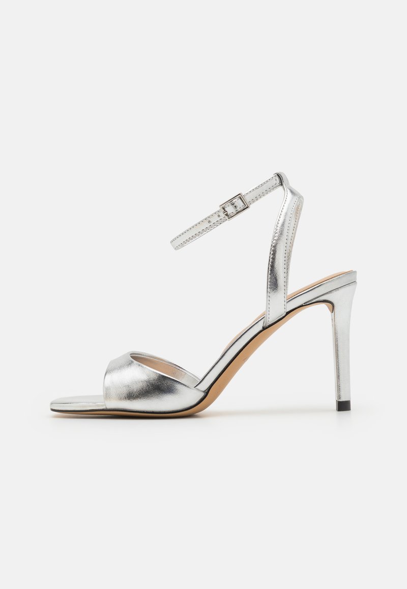 Sandale à talon haut argentée avec un bout ouvert, texture métallique et bride de cheville ajustable. Présente un talon aiguille effilé et une semelle intérieure lisse.