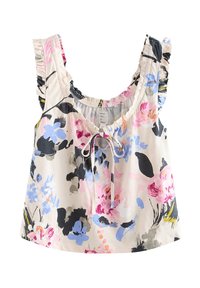 Top court blanc sans manches avec imprimé floral rose, bleu et noir, bretelles à volants et un détail de lien noué devant au niveau de l’encolure.
