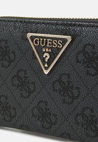 Czarny portfel o teksturowanej powierzchni z złotym trójkątnym logo Guess, z delikatnym wzorem wytłoczonym na powierzchni. Zamek błyskawiczny na górze.