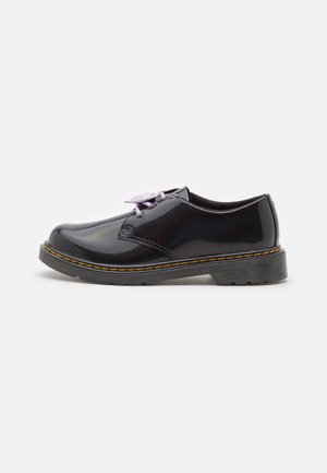 Scarpa oxford in pelle verniciata nera con suola spessa, cuciture gialle e lacci lavanda su sfondo bianco.