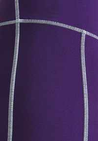 Fialová tkanina s hladkou texturou, se zajímavým bílým prošíváním v geometrickém vzoru. Design zahrnuje segmentované panely a kontrastní švy.