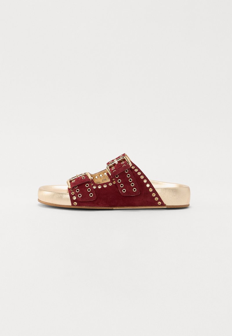Sandales à glissière en suede rouge avec deux sangles à boucle, ornées de clous dorés, et une semelle métallique dorée. Design plat, silhouette ouverte.
