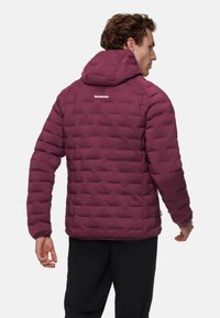 Burgundowa kurtka puchowa z kapturem, z pikowanym wzorem i elastycznymi mankietami. Tył z białym logo "MAMMUT".