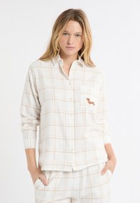 Biała flanelowa koszula w brzoskwiniową kratę, z przodem zapinanym na guziki oraz kieszenią na piersi ozdobioną haftowanym wzorem jamnika. Długie rękawy.