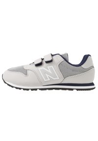 Ljusgrå sportskor med marinblå accenter, nätpaneler och kardborreband. Har en tjock svart gummisula och en framträdande "N"-logotyp.