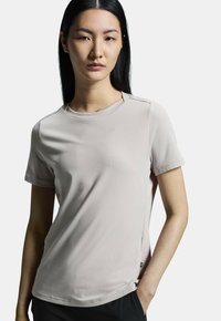 Camiseta de manga corta color beige claro con una textura suave, cuello redondo, detalles de costura sutiles y una pequeña etiqueta de logo en el lado inferior.