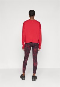 Rød langermet hettegenser med en kortet design, kombinert med tettsittende svarte leggings med et rødt og svart sprutmønster. Svarte treningssko.