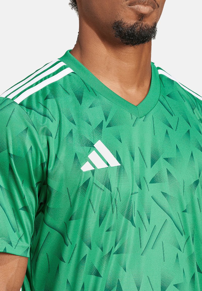 Grünes Sporttrikot mit einem strukturierten Muster aus dreieckigen Formen. Verfügt über einen V-Ausschnitt und drei weiße Streifen auf den Schultern.