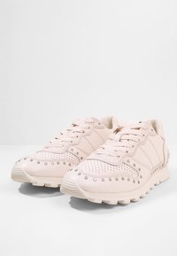 Světle růžové sportovní tenisky s perforovanými detaily, kulatou špičkou a texturovanou podrážkou. Disponují šněrovacím designem a kovovými akcenty po stranách.