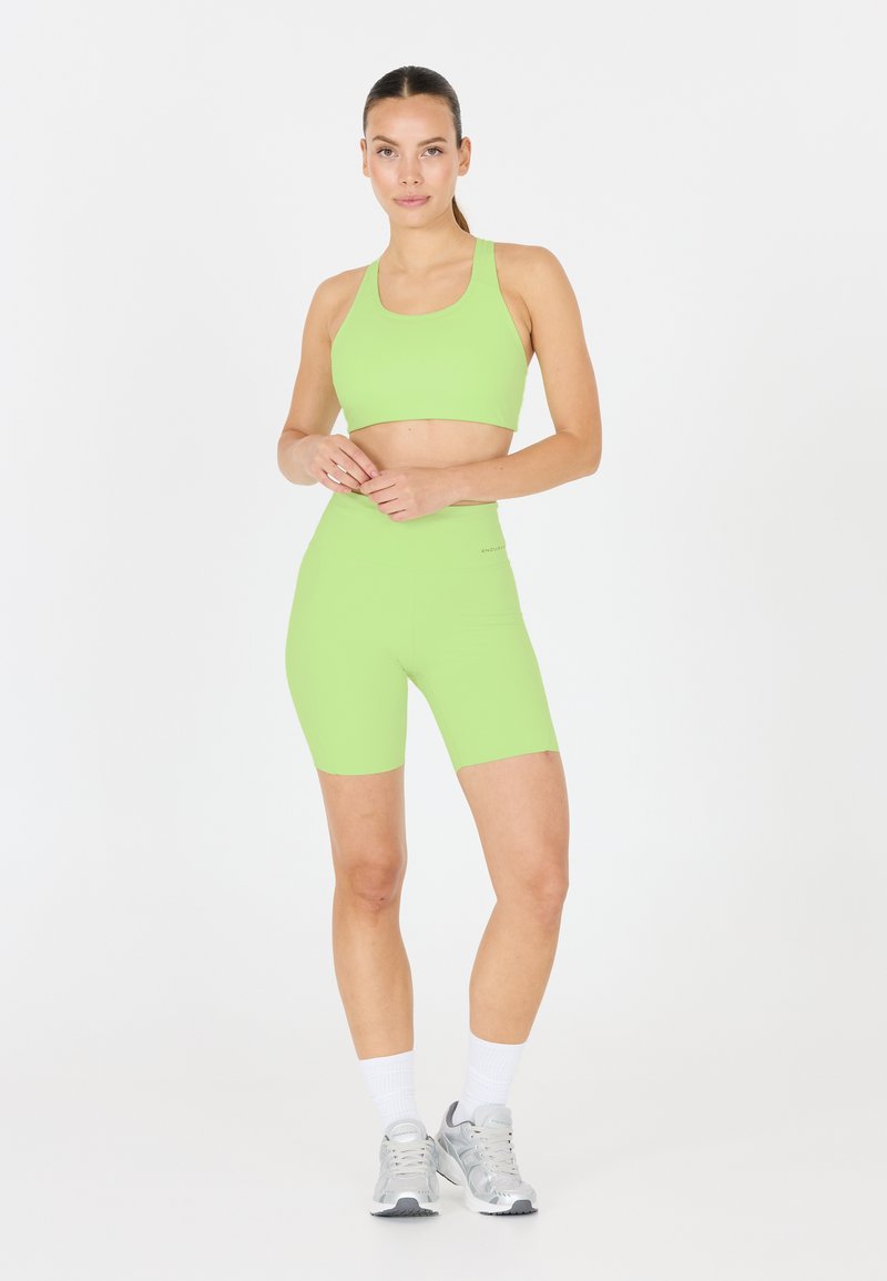 Neon grön atletisk crop top och shorts set, tillverkat av mjukt, elastiskt tyg. Modellen bär silverfärgade atletiska skor och vita ankelsockor.