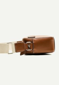 Brown leather bag with a rectangular shape, featuring a thick cream strap and silver hardware detail. Smooth texture with neat stitching.