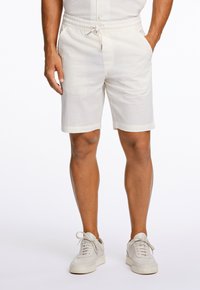 Witte textuurshorts voor mannen met een elastische tailleband en aantrekkoord. Heeft zijzakken en een rechte zoom. Gepaard met lichte sneakers.