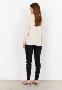 Maglione beige a maglia con maniche lunghe, abbinato a jeans skinny neri e sandali con tacco stampa leopardata. Modella vista da dietro.