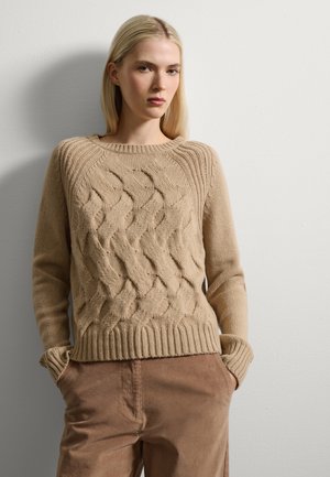 Maglione beige lavorato a maglia con un motivo a trecce testurizzato, colletto e polsini a coste, indossato sopra pantaloni in velluto a coste marroni. Tessuto morbido, vestibilità casual.