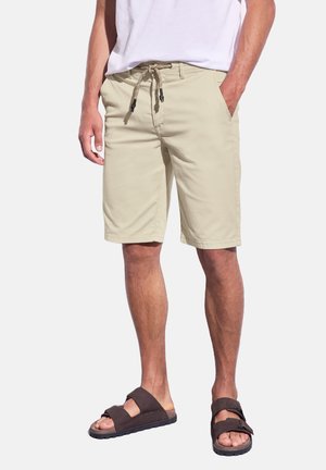 Pantaloni corti beige con vita elastica e cordoncino. Presentano due tasche laterali e una vestibilità dritta, abbinati a sandali marroni.