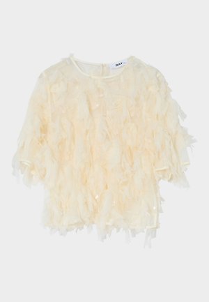 Blouse crème à manches courtes avec des bandes de tissu superposées créant un effet texturé et duveteux, avec un col rond et une fermeture éclair au dos.
