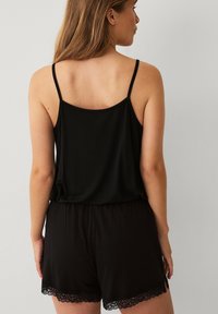 Zwarte tanktop met dunne banden en een losse pasvorm, gecombineerd met zwarte shorts met kantafwerking aan de zoom. Glad fabric met een ontspannen ontwerp.