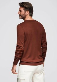 Bruine geribbelde trui met lange mouwen en een ronde halslijn, gecombineerd met crème cargo broek. Glad textuur en aangesloten ontwerp.