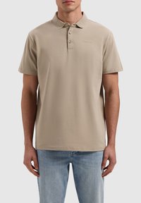 Beige poloshirt met korte mouwen, gemaakt van zacht materiaal. Met een drieknoopsluiting en subtiele logo borduring op de borst.