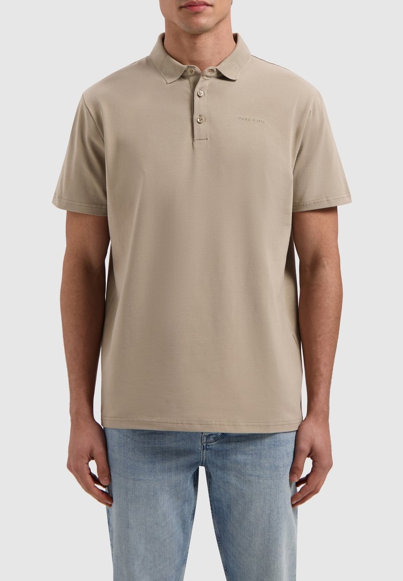 Beige poloshirt met korte mouwen, gemaakt van zacht materiaal. Met een drieknoopsluiting en subtiele logo borduring op de borst.