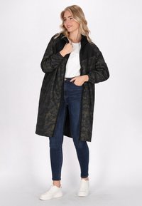 Cămașă cu camuflaj negru și verde închis, lungă și lejeră, cu fermoar în față, mansete elastice și o textură fină. Purtați peste blugi și adidași.