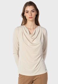 Hochgeschlossener Langarm-Top in hellem Beige, aus weichem Stoff mit Drapierung am Halsausschnitt und schmalen Ärmeln.