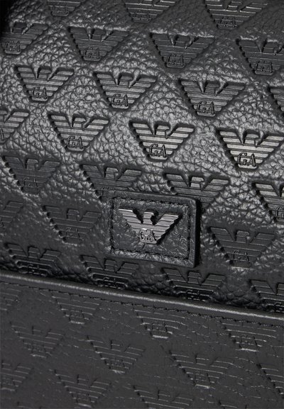 Surface en cuir noir texturé embossée de logos d'aigles stylisés répétés et une plaque métallique de logo au centre.
