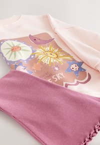 Rosa tröja med färgglada blommönster och stjärnor, tillsammans med en texturerad rosa halsduk. Tröjan har ribbad halsringning och fåll.