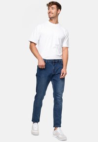 Siniset farkut slim-fit-leikkauksella ja viiden taskun suunnitelmalla, yhdistettyinä yksinkertaiseen valkoiseen puuvillapaitaan ja valkoisiin lenkkareihin. Rento asu.