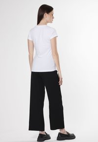 Camiseta blanca de manga corta combinada con pantalones de pierna ancha negros. Llevada con zapatos negros con un acento decorativo. Tejido suave y casual.