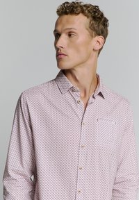 Helles rosa Langarmhemd mit geometrischem Muster, Button-Down-Kragen und einer Brusttasche mit dezentem Logo. Aus weichem Baumwollstoff.