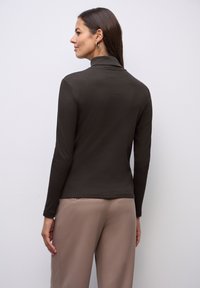 Brązowy długi rękaw z wysokim kołnierzem, o gładkiej fakturze i dopasowanym kroju, w połączeniu z jasnobeżowymi spodniami typu wide-leg.