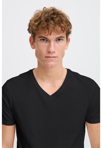Tricou negru cu guler în V dintr-un material moale și neted. Mâneci scurte, croială slim și design minimalist, fără modele sau accente suplimentare.
