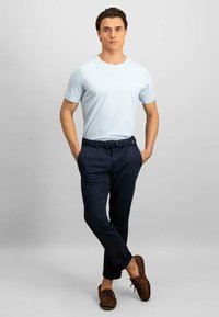 Tricou bleu deschis cu mâneci scurte, asortiat cu pantaloni navy, o curea țesută navy și pantofi din piele maro, pe un fundal neutru.
