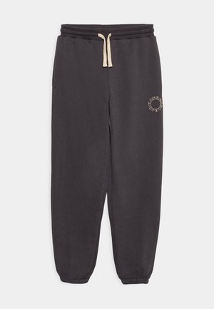 Pantalones deportivos gris oscuro con puños elásticos, cintura con cordón crema, bolsillos laterales y pequeño logo circular en la parte superior del muslo izquierdo.