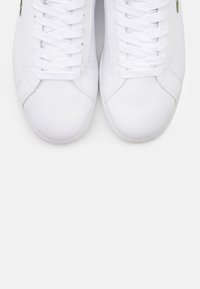 Un paio di scarpe da ginnastica in pelle bianca pulite con lacci bianchi, viste dall'alto su uno sfondo bianco semplice.