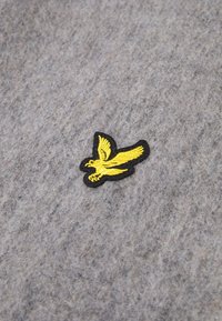 Tessuto grigio con una texture morbida, caratterizzato da un ricamo di un uccello giallo bordato di nero. I punti dettagliati sono ben visibili sullo sfondo.