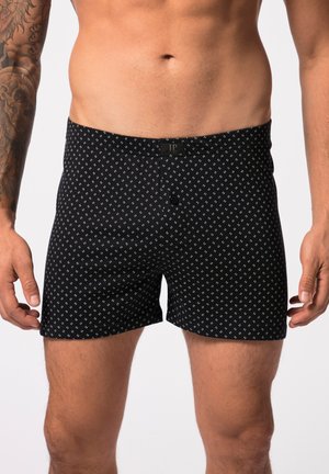 Zwarte boxershorts met wit geometrisch patroon, knoopsluiting en elastische tailleband. Stof lijkt glad met minimale textuur.
