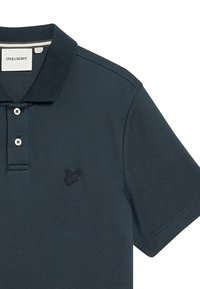 Mörkblå pikétröja i bomull, med treknappsknäppning, korta ärmar och en broderad logotyp på vänster bröst.