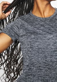 Szara dopasowana koszulka z krótkim rękawem, o melanżowym, fakturowanym wzorze; posiada okrągły dekolt oraz delikatnie zaokrąglony dół.