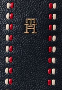 Portofel din piele albastru închis, cu un logo auriu și studs decorative în roșu și alb, aranjate în linii verticale de-a lungul marginii.