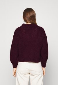 Burgundy stickad tröja med en tjock textur, ribbade muddar och hög krage. Kortherr design med rak fåll och lös passform.