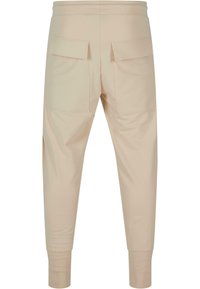 Beige joggebukser laget av mykt stoff, med to baklommer, smalere ben og ribbede mansjetter ved anklene for en tettsittende passform.