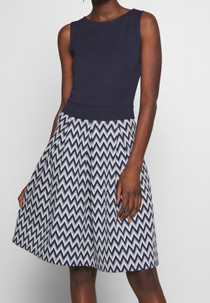 Robe sans manches avec un corsage bleu marine et une jupe évasée avec un motif en zigzag bleu marine et blanc, réalisée dans un tissu lisse.