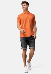 Oranje poloshirt met kraag, gecombineerd met grijze opgerolde shorts en witte sneakers. Eenvoudig, casual ontwerp met een gestructureerde afwerking.