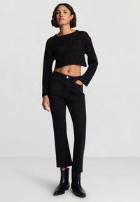 Maglione nero corto in maglia con lavorazione aperta, abbinato a jeans neri a gamba dritta e stivaletti neri. Texture piatta e liscia su tutta la superficie.